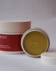 A small, open jar of Golden Body Butter is leaning against a closer large jar of Golden Body Butter. It's rich, thick texture and golden colour shimmer.