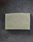 The organic Cedarwood and Sage soap bar sits on a stone plate in the shadow of ferns.