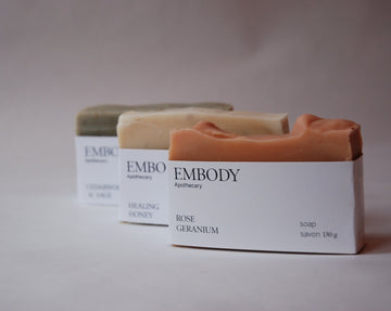Three luxury hand crafted soap bars sit in a diagonal line, Rose geranium, Healing Honey, and Cedar wood and Sage.