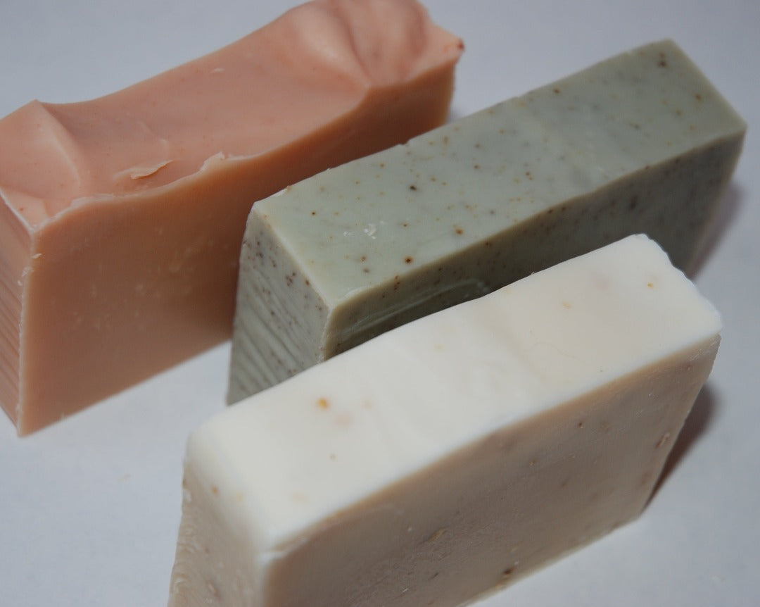 Three luxury hand crafted soap bars sit in a diagonal line, Rose geranium, Healing Honey, and Cedar wood and Sage.