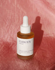 The Botanical Facial Serum sits on a hand-dyed pink silk scarf.