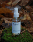 The handcrafted, all natural Rosewater Facial Toning Mist, made with pure Rose hydrosol, sits on a bed of moss in a forest.
