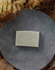The all-natural cedarwood and sage soap bar sits on in a bed of ferns in a forest.